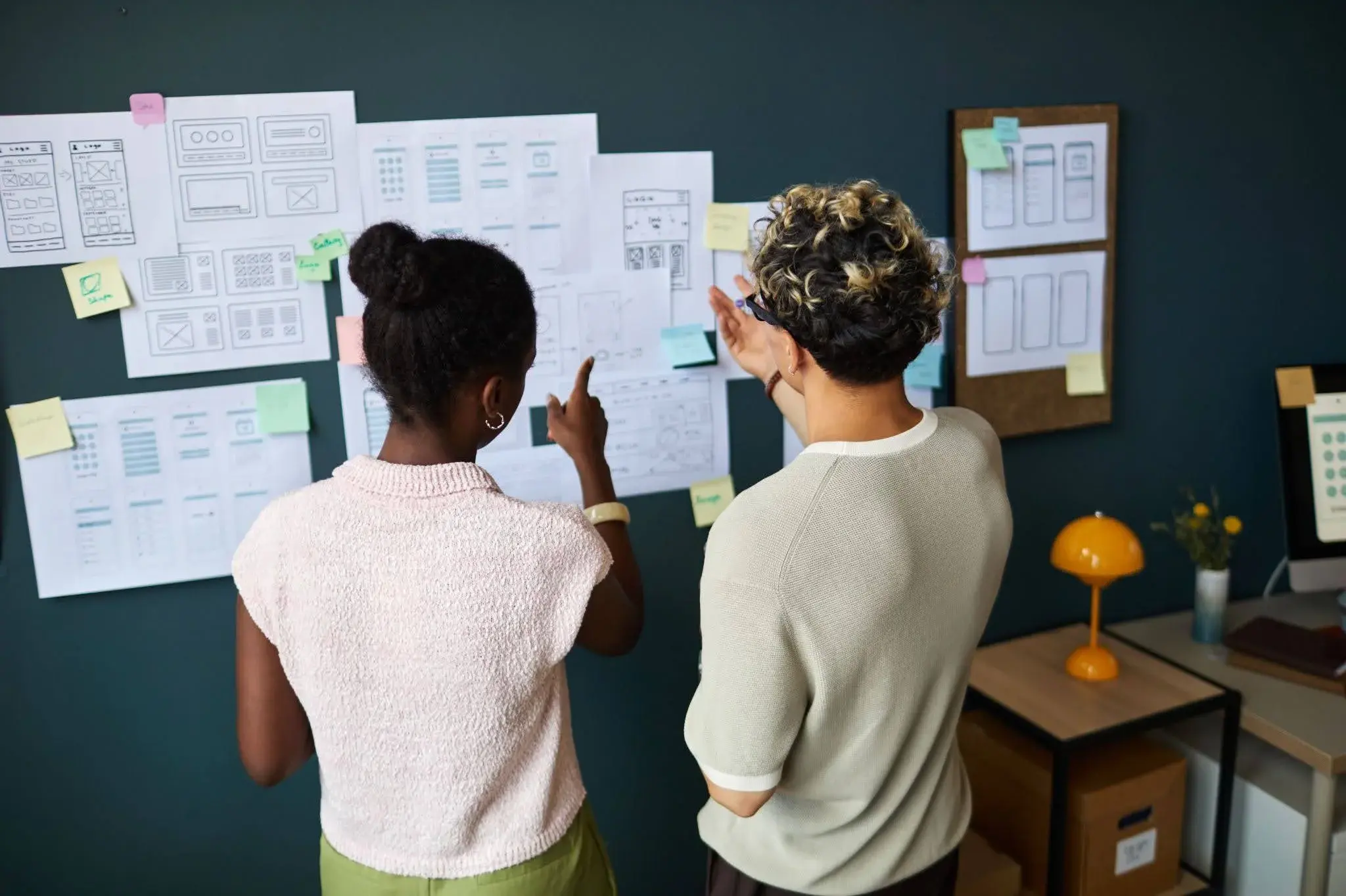 Two people looking at papers on a wall, and trying to put together an apprenticeship plan without the help and support of professionals.