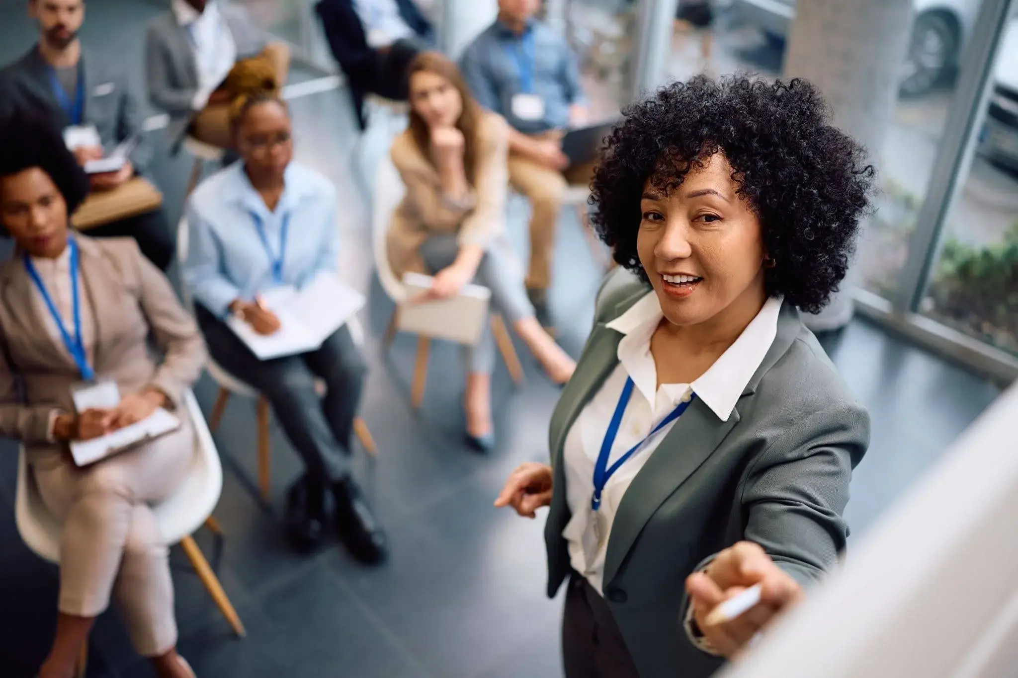 A woman training improvement practitioner apprentices, pointing at a board with a white pen. 
